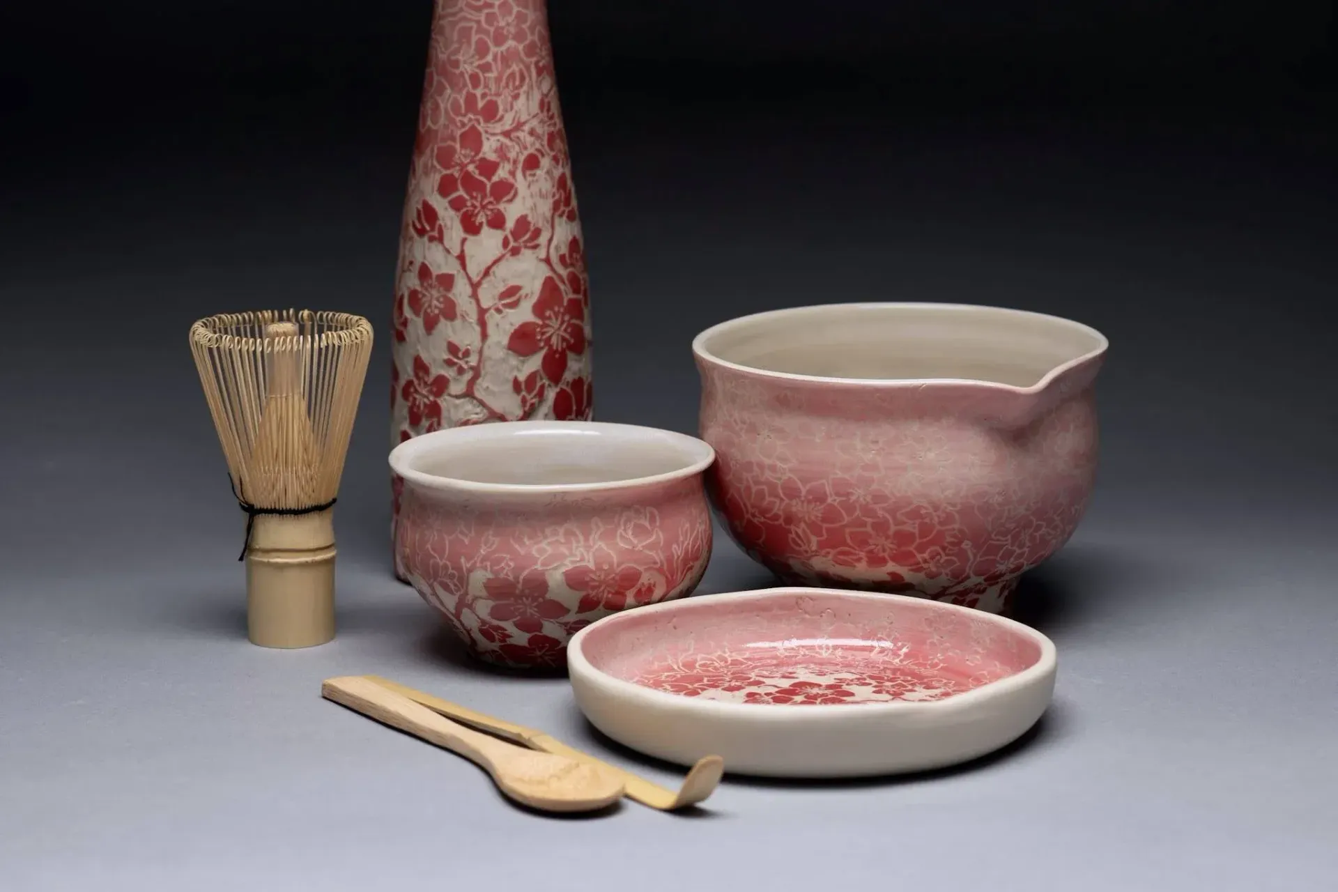 Matcha tea ceremony set with red-patterned ceramics, bamboo whisk, spoon, and chashaku.