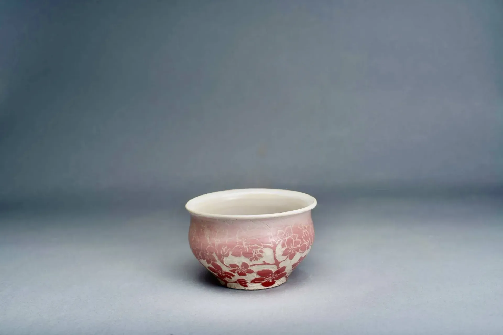 Pink and white pottery bowl with cracked exterior, set against a gray backdrop.