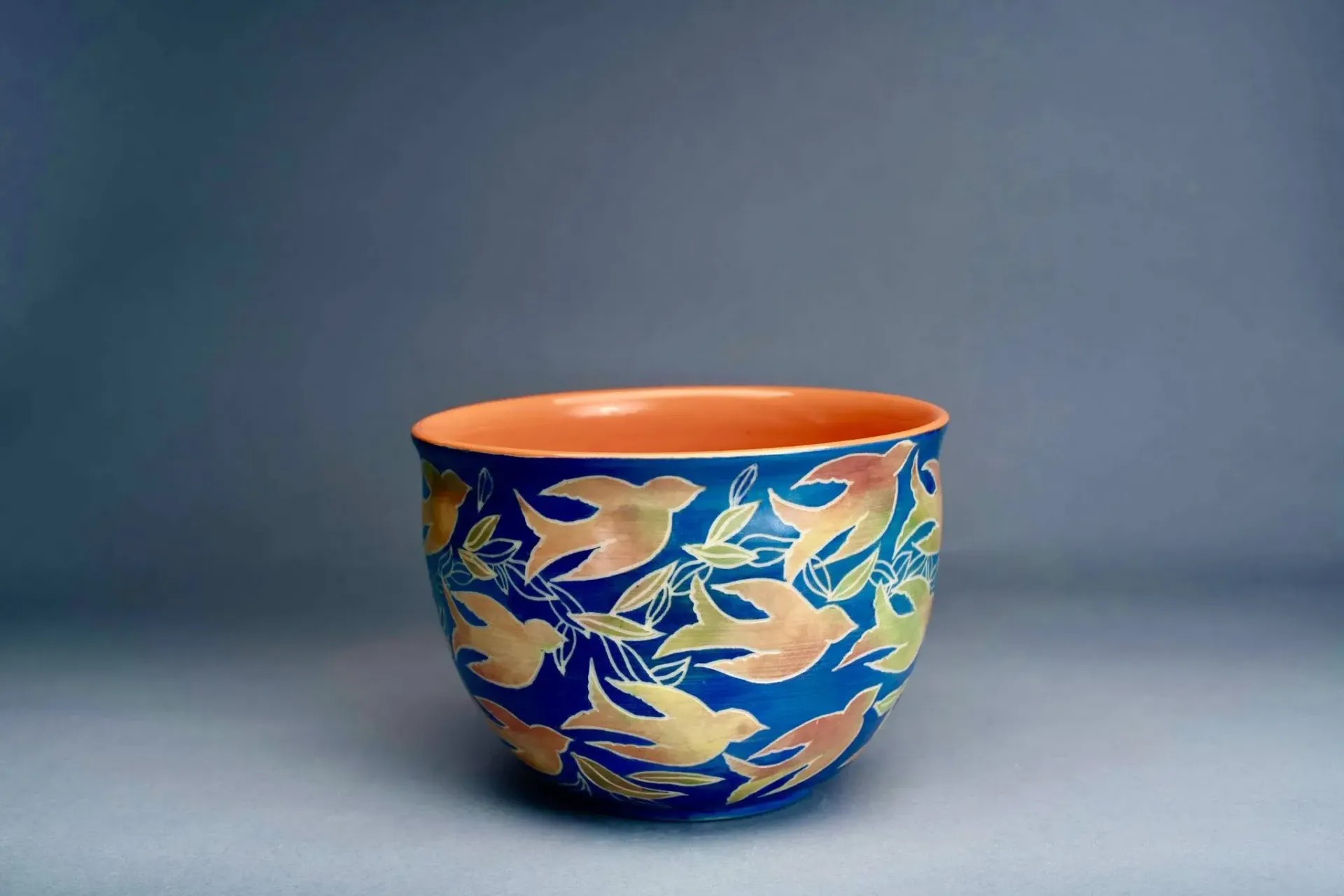 Ceramic bowl with blue background and gold/orange leaf design, orange interior.