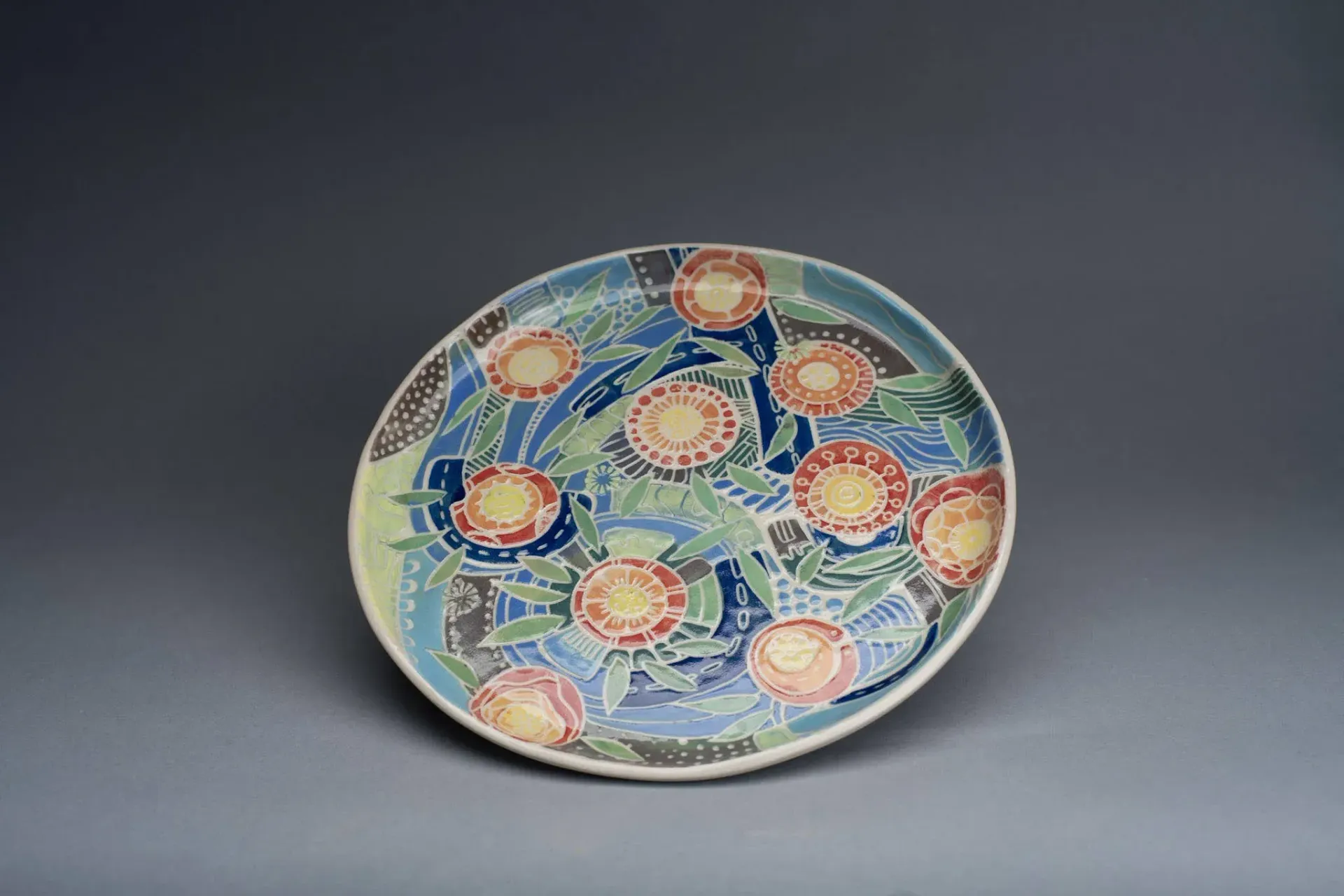 Decorative ceramic plate with floral design; red, orange, blue, and green hues.