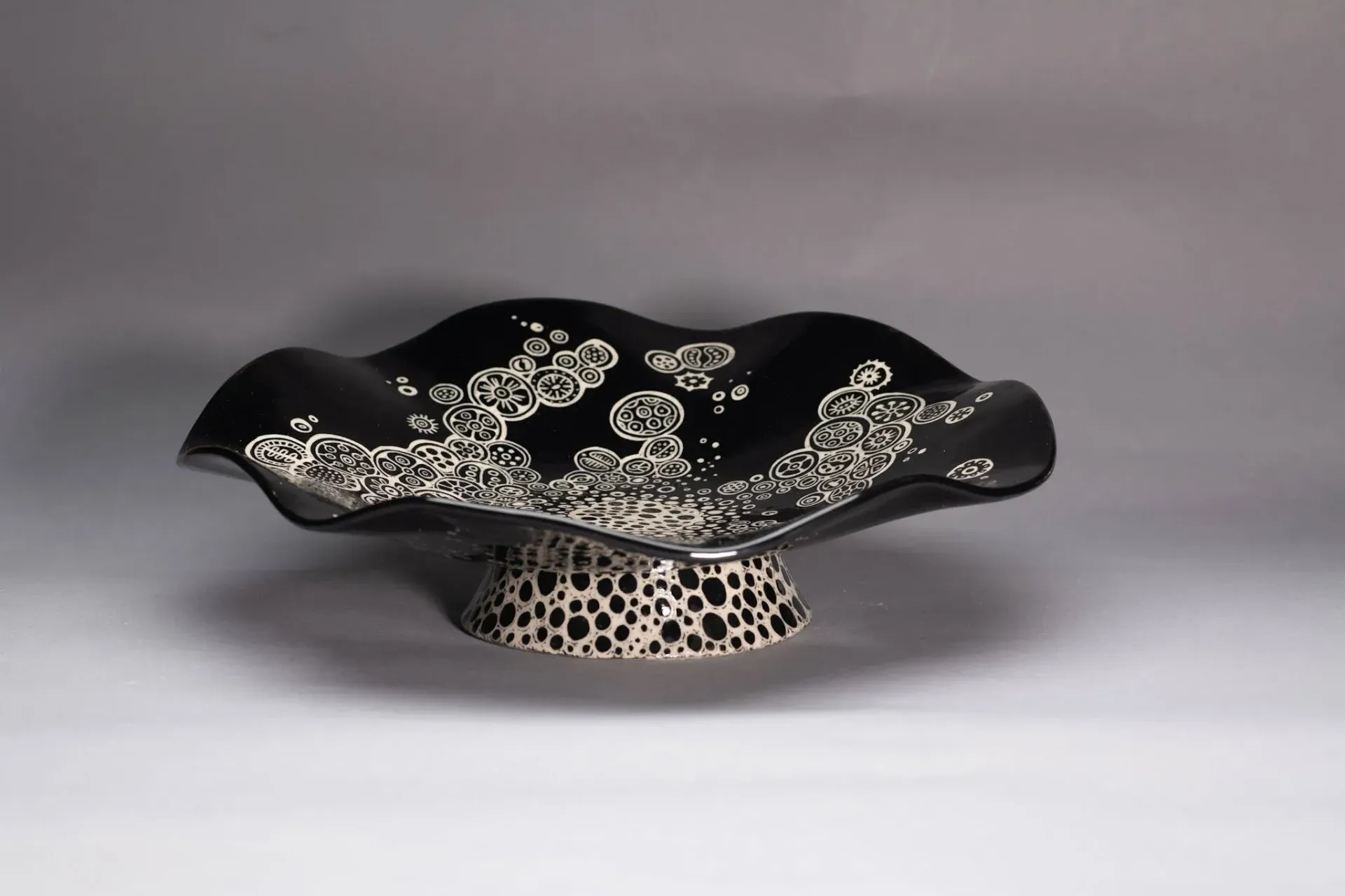 Black and white ceramic cake stand with a wavy rim and patterned base.