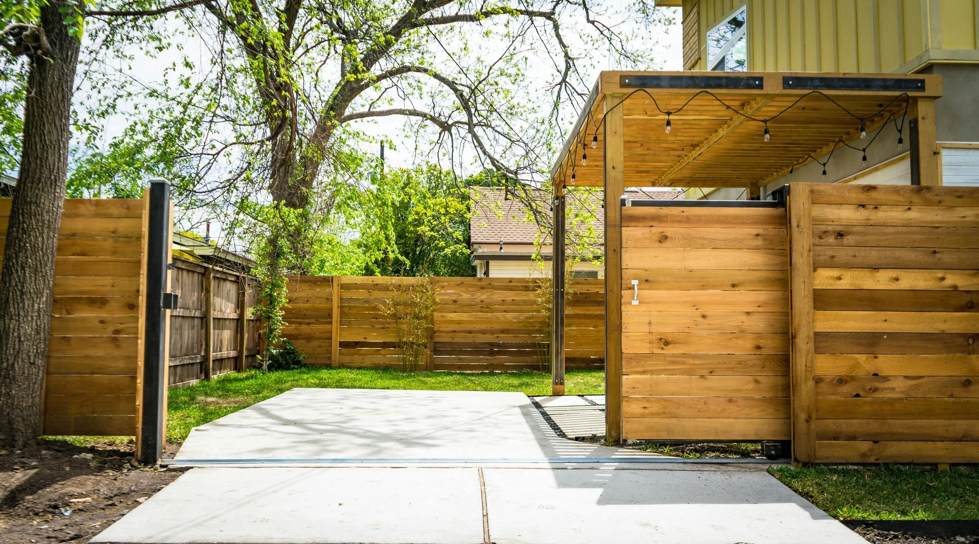 A wooden fence surrounds a concrete driveway leading to a house.
