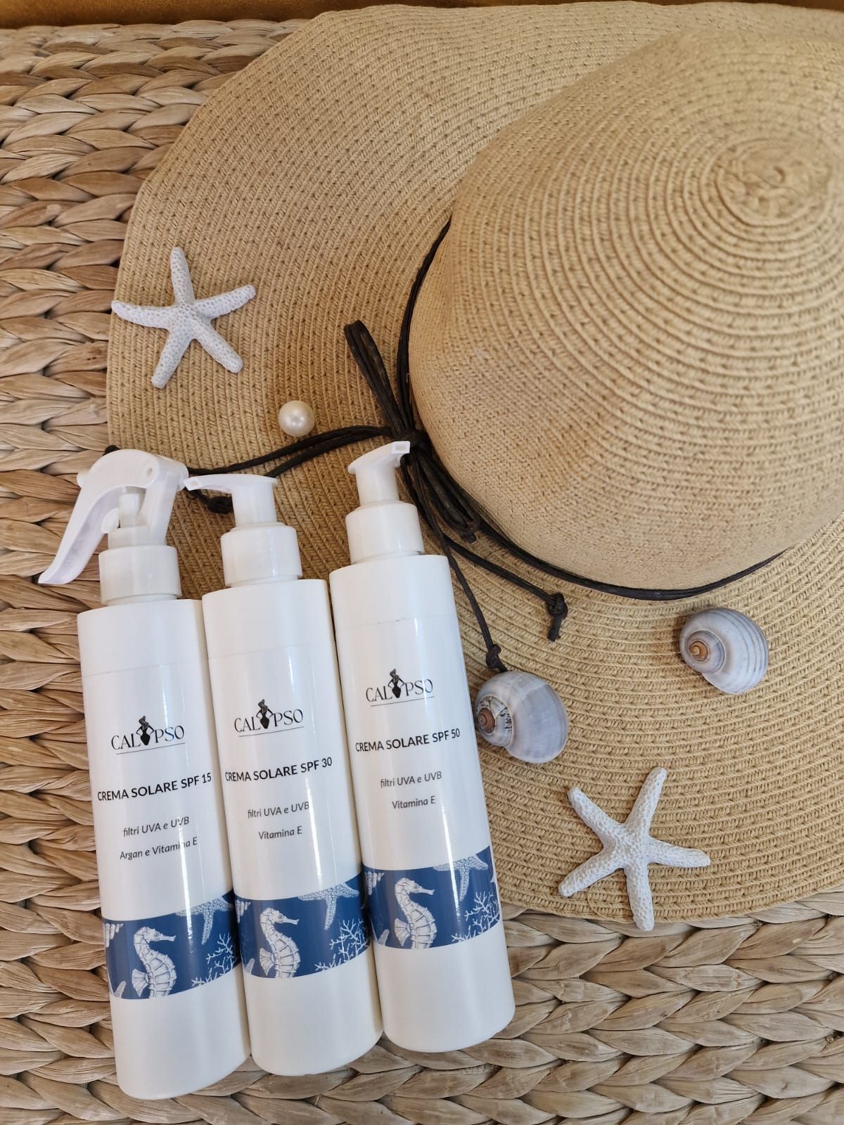 Tre bottiglie spray sono appoggiate su una stuoia di vimini, accanto a un cappello e una stella marina.