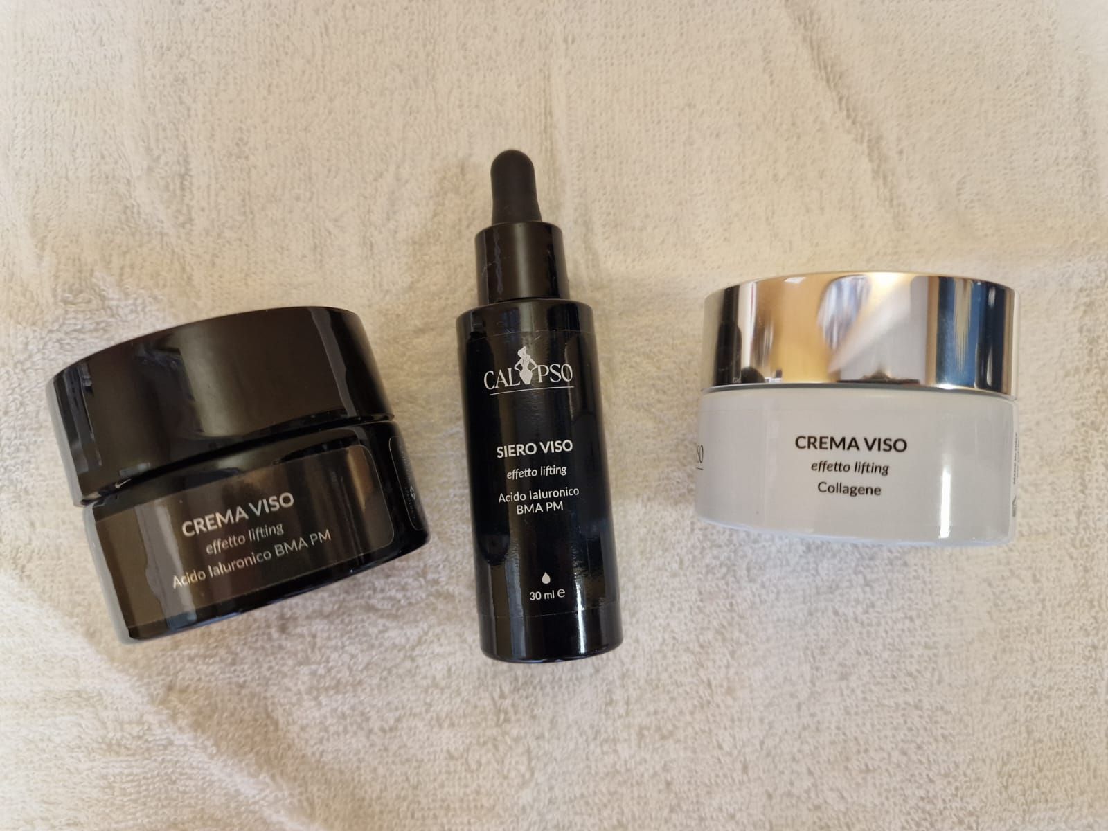 Tre bottiglie di cosmetici sono appoggiate su un asciugamano bianco.