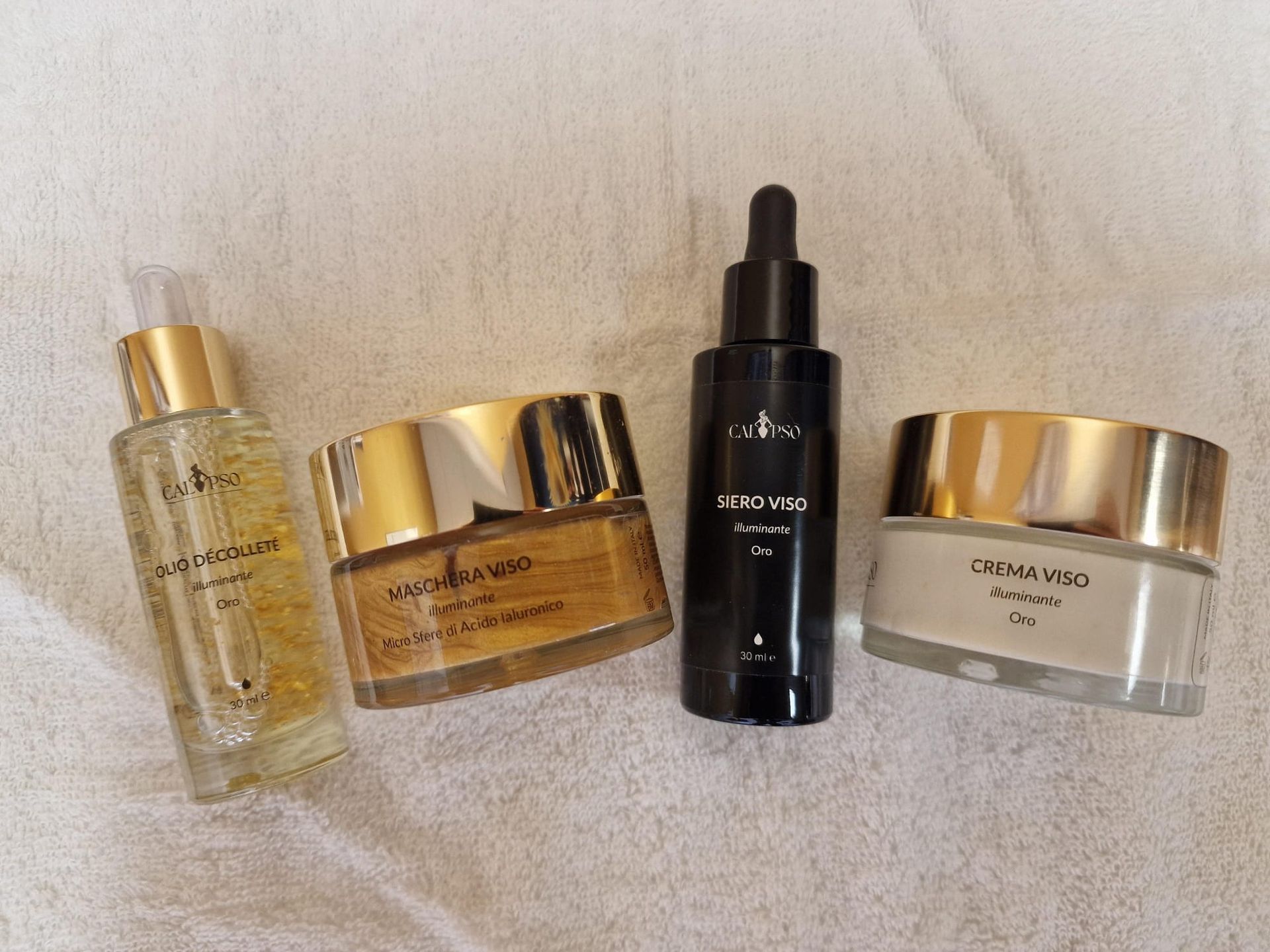 Quattro flaconi di cosmetici sono appoggiati su un asciugamano bianco.