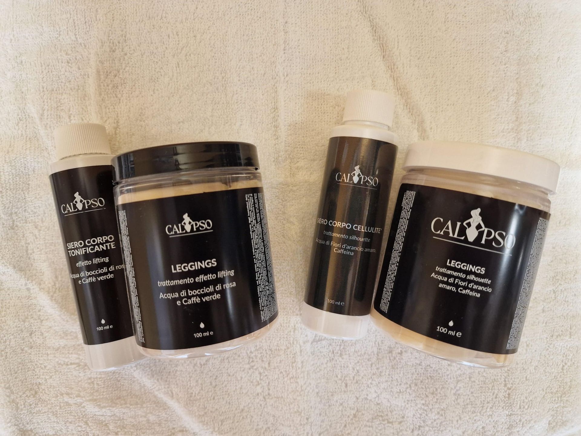 Quattro flaconi di cosmetici sono appoggiati su un asciugamano bianco.