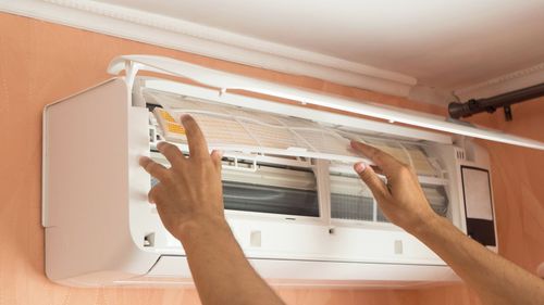 A person is cleaning an air conditioner with their hands.