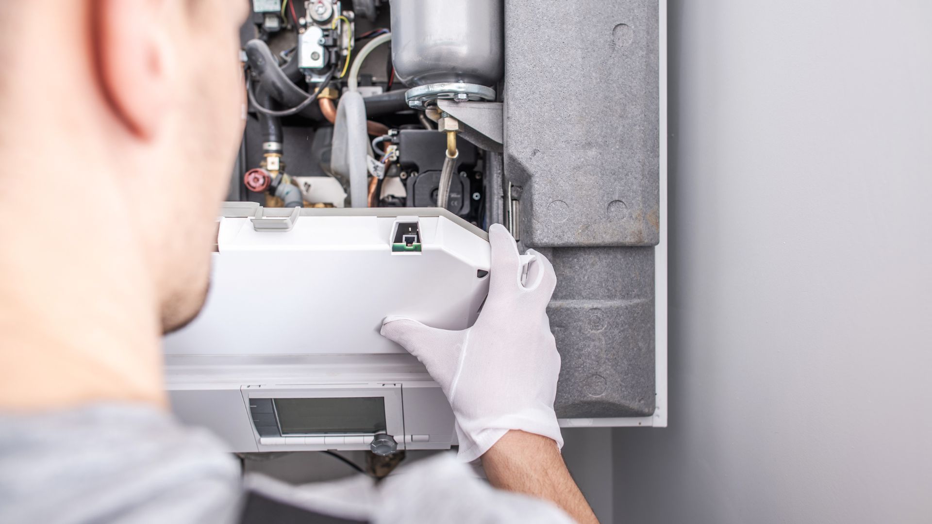 A man wearing white gloves is working on a boiler.