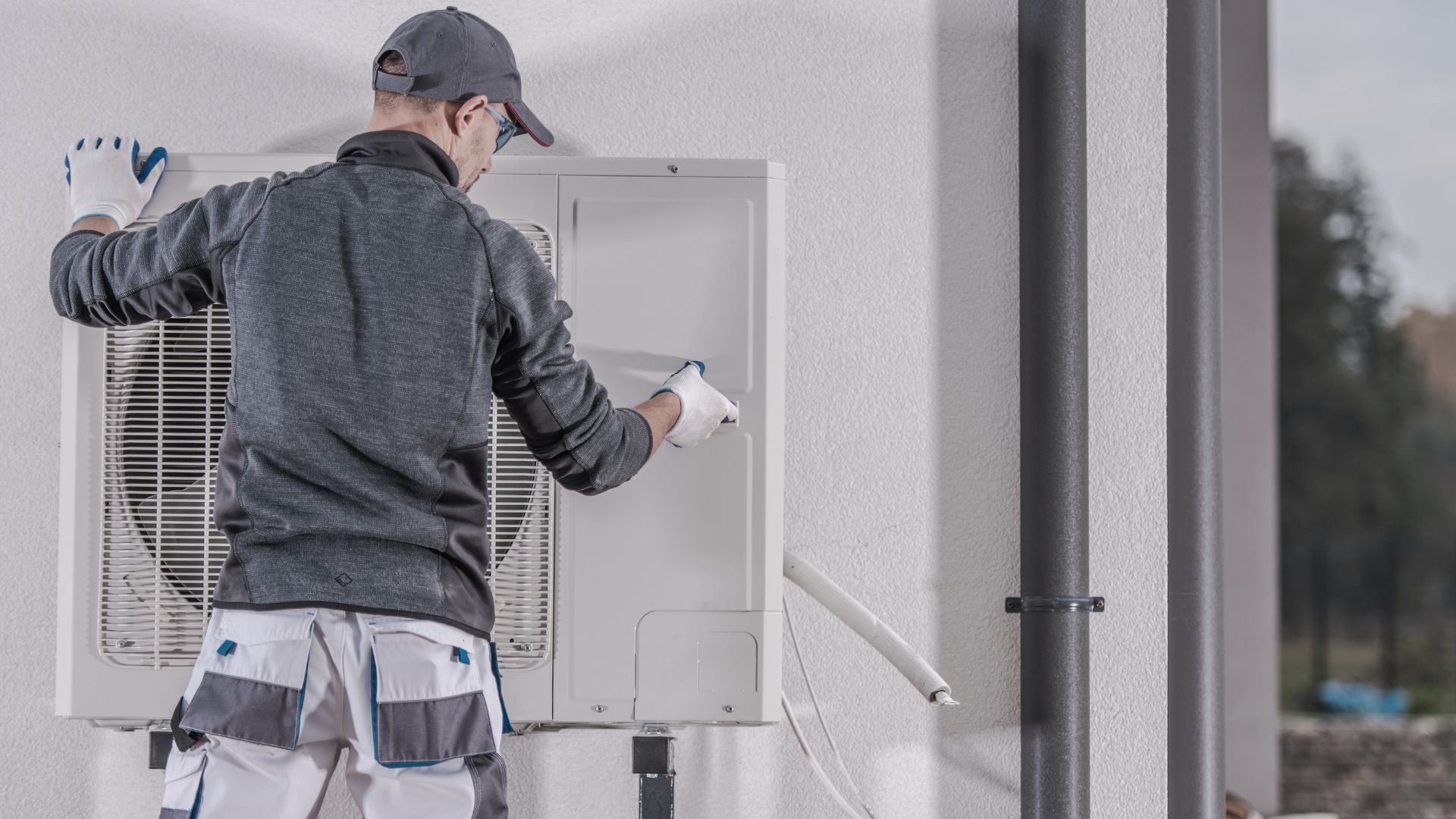 A man is installing an air conditioner on the side of a building.