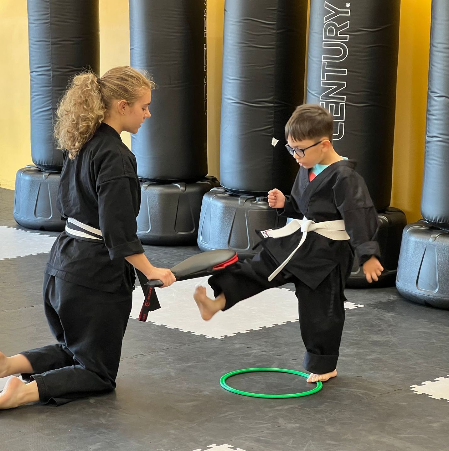 Young Child kicking a pad that a female instructor is holding. The image links to the Junior Dragons Martial Arts Page.