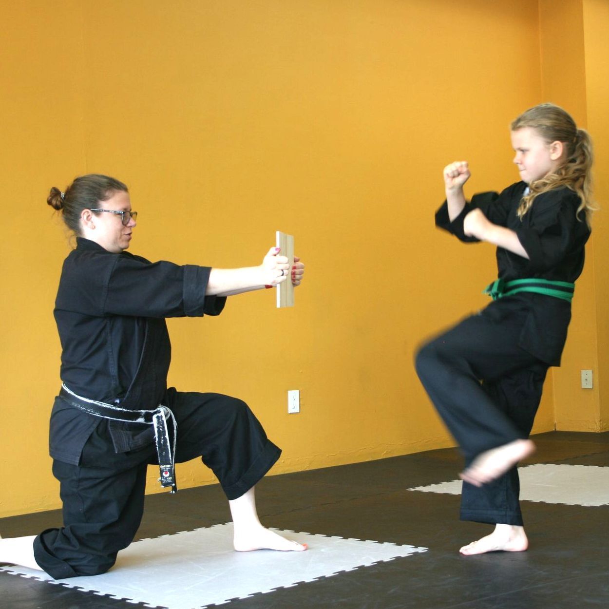Two women in black karate uniforms are practicing martial arts