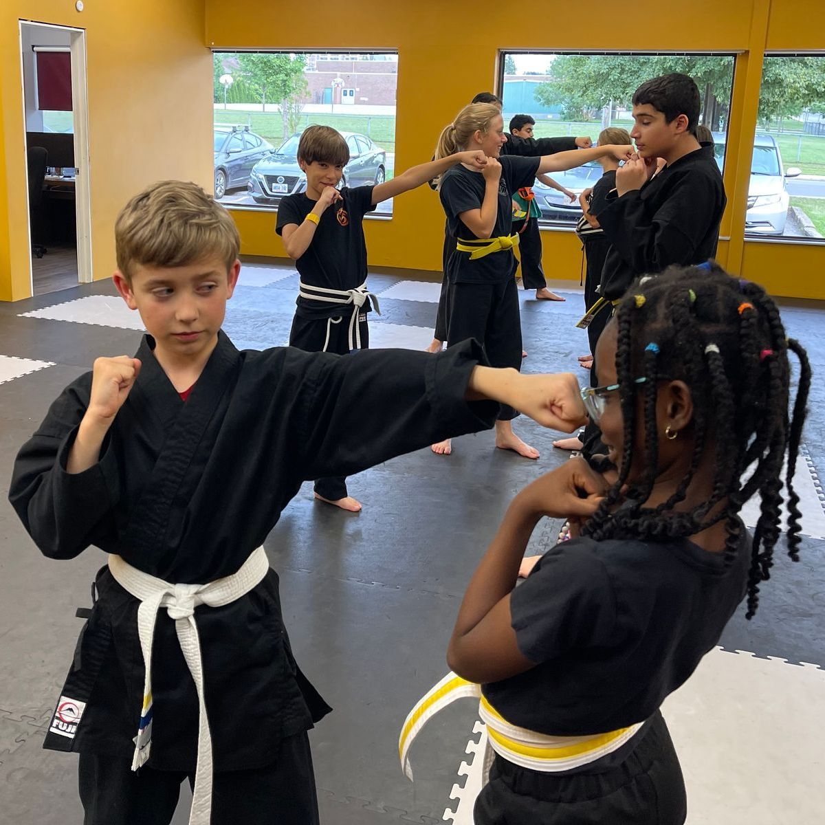 A group of kids are practicing martial arts in a gym. The image links to the Kids Martial Arts Program page.
