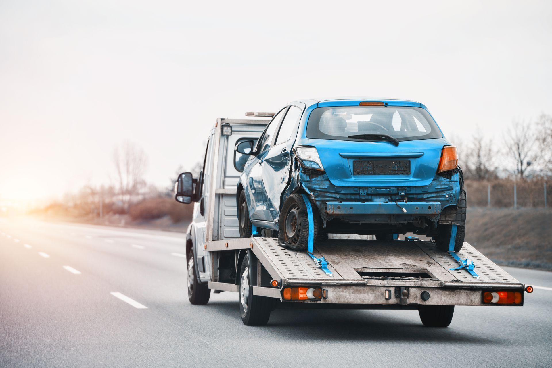 Blue, damaged car loaded onto a tow truck on a highway.