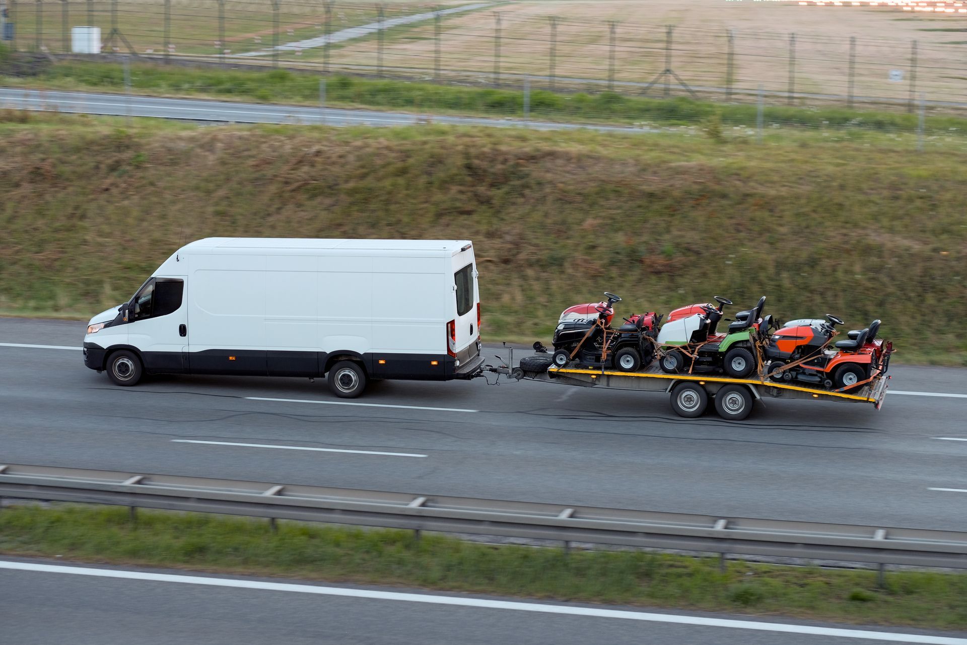 Road roller on the back of a flatbed truck, parked on a road. Blue sky.