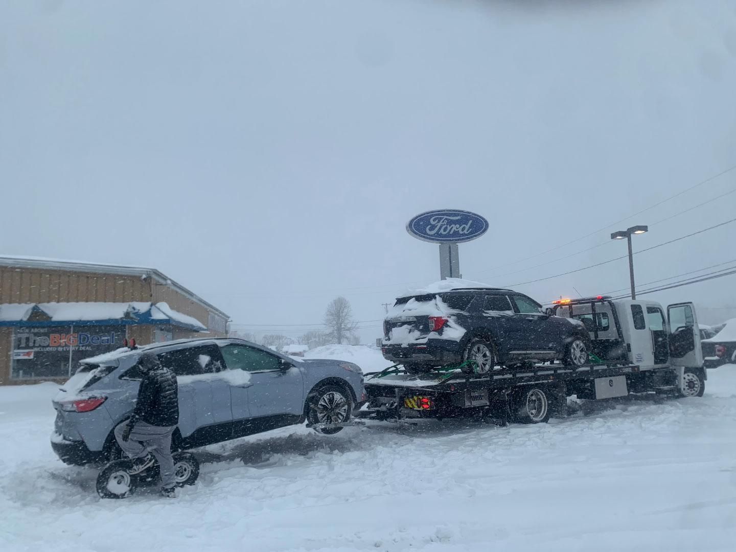 White SUV towing a white caravan on a paved road, surrounded by trees.
