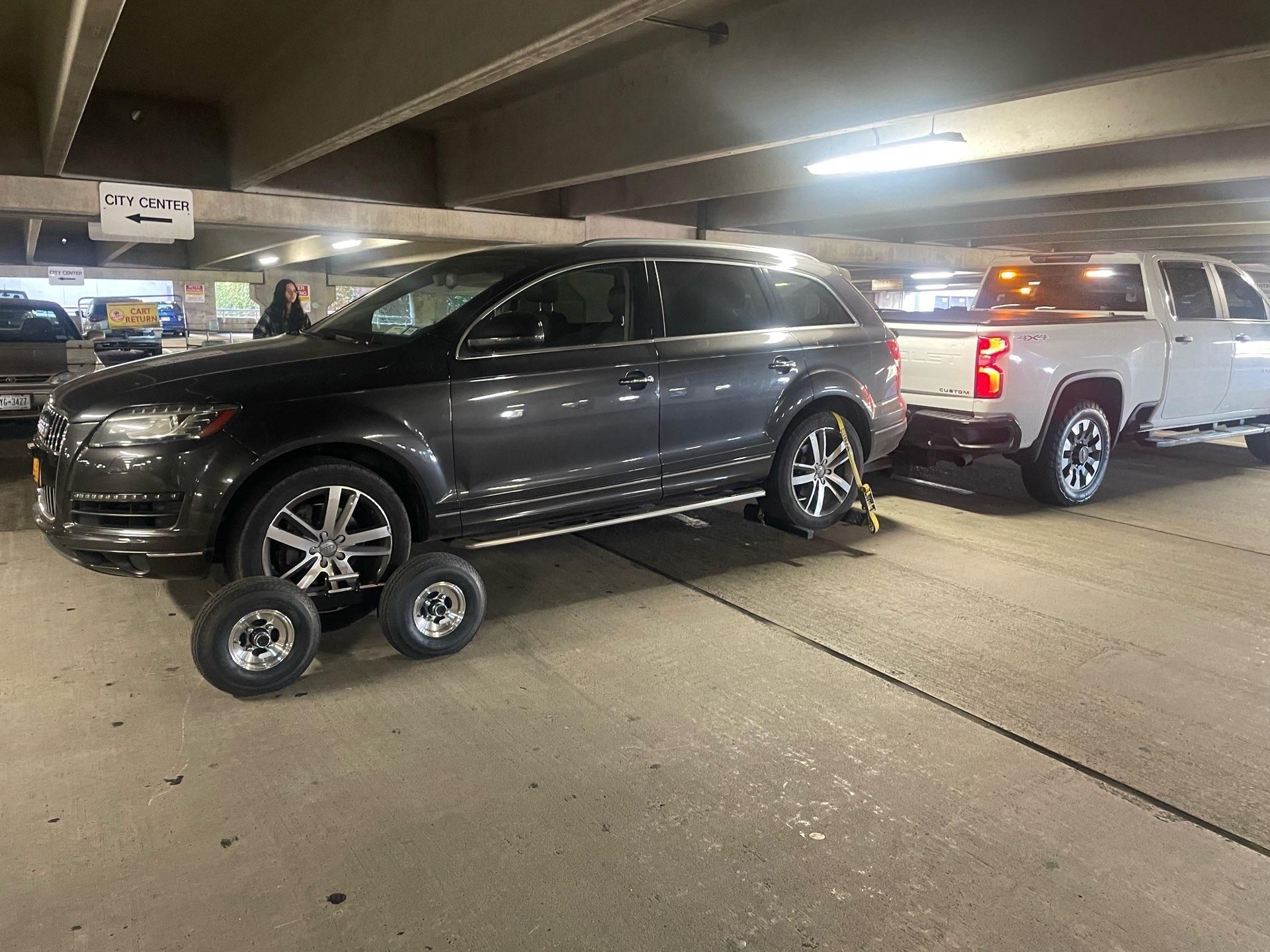 White car being loaded onto a tow truck on a roadside, silver ramp visible.