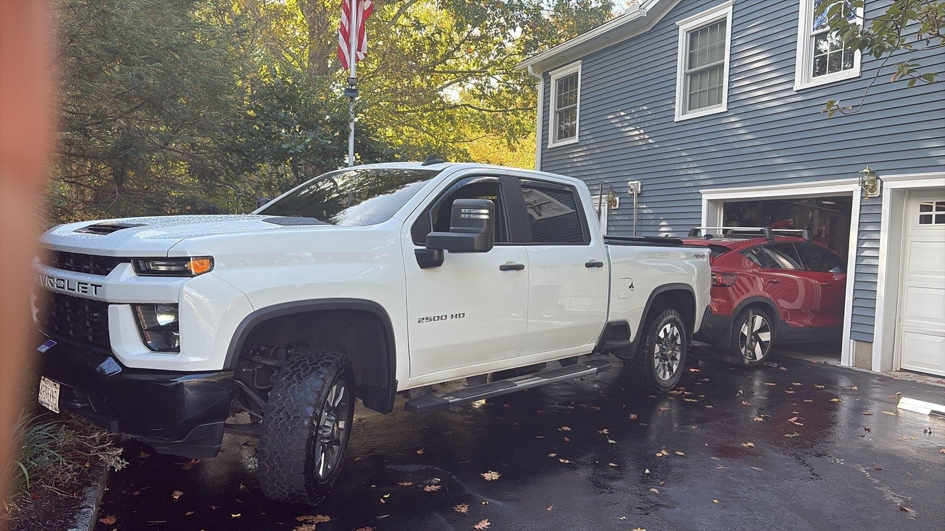 Blue car's rear with a trailer hitch, parked on a street; other cars blurred in the background.