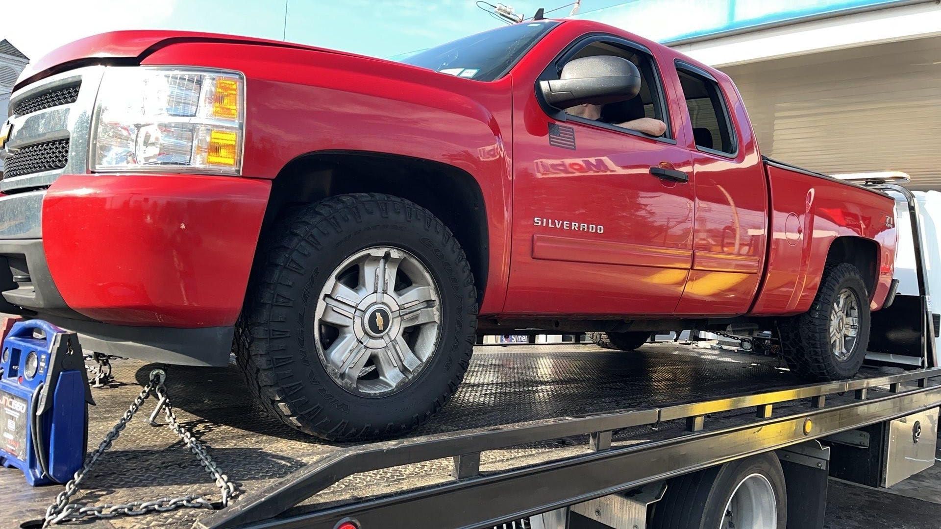 Damaged silver car with a man crouching on the sidewalk, looking distraught.