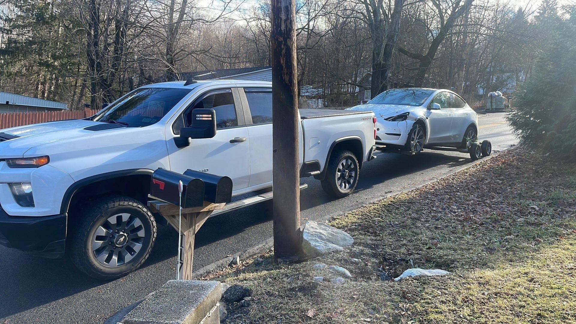 Tow truck operator loading a white car onto the flatbed; forest background.