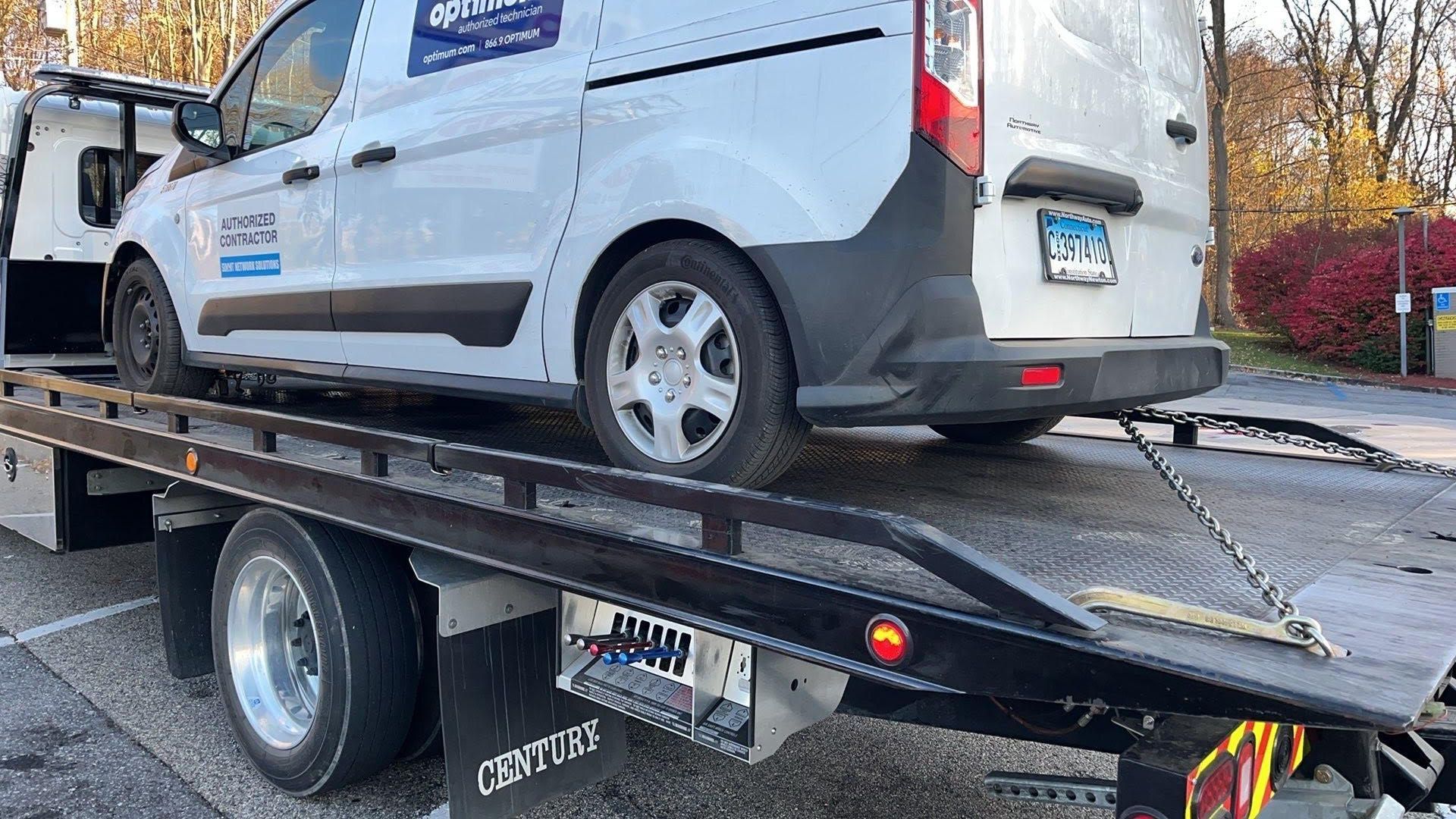 Tow truck towing a white SUV on a city street.