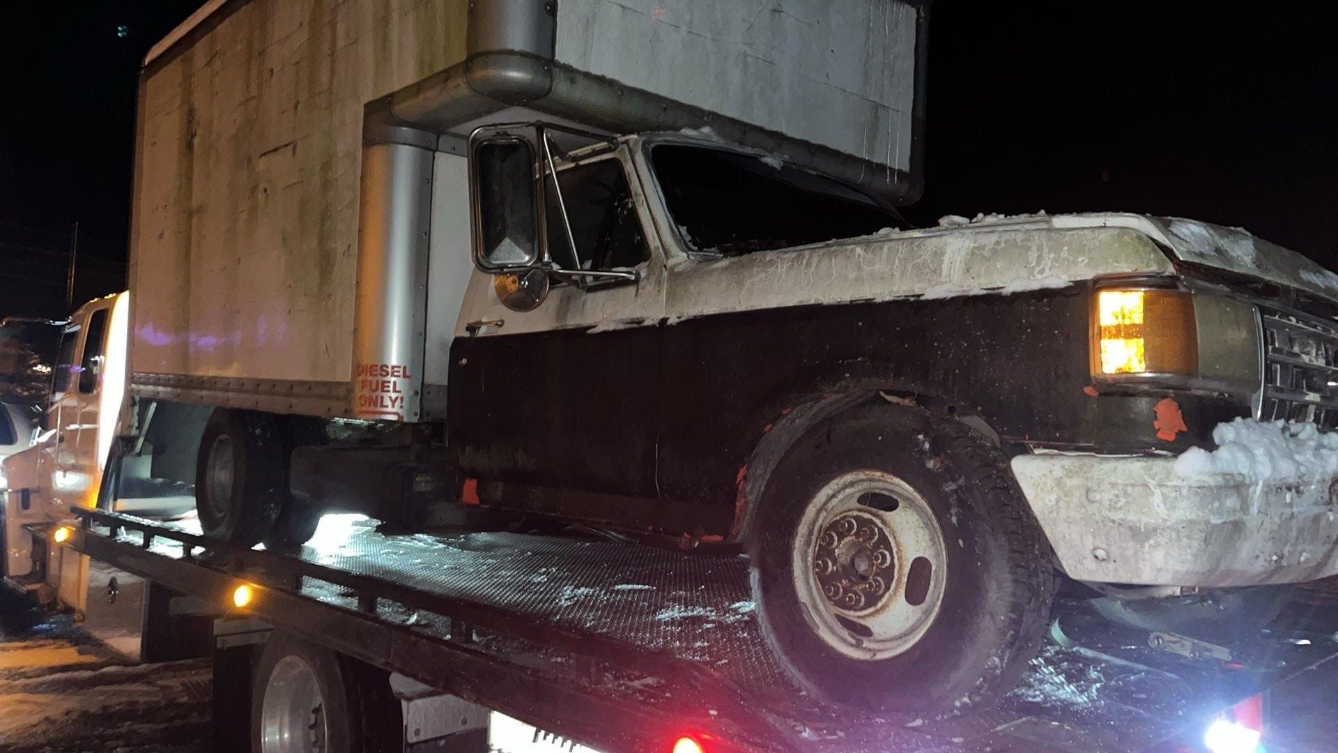 Person inspecting a red SUV with an open hood, parked on the side of a road, near a field and trees.