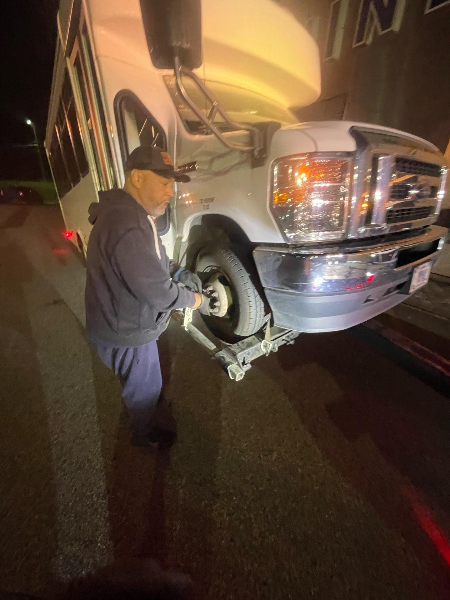Woman in blue denim shirt standing by car with open hood, looking at phone.