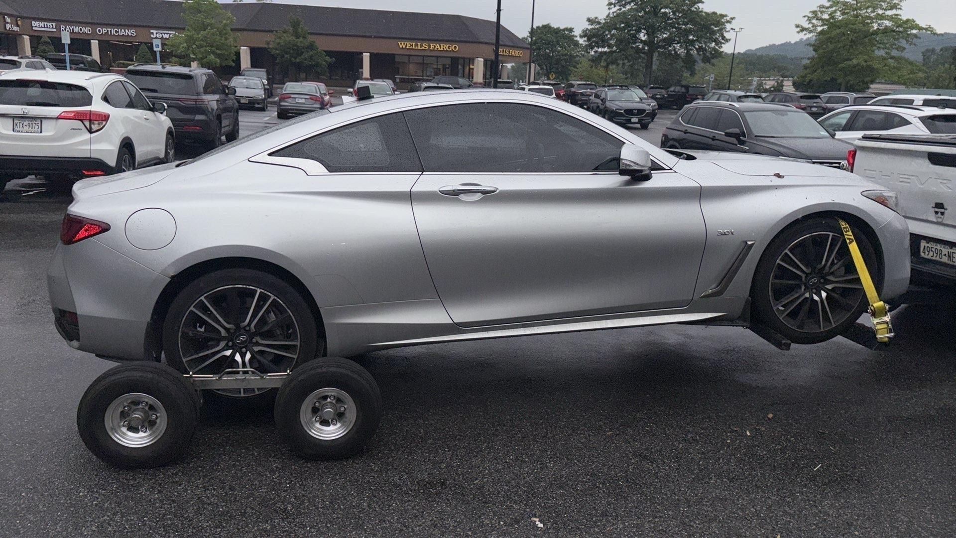 Person connecting trailer hitch to a vehicle. Outdoors, gray vehicle and trailer, person in plaid shirt.