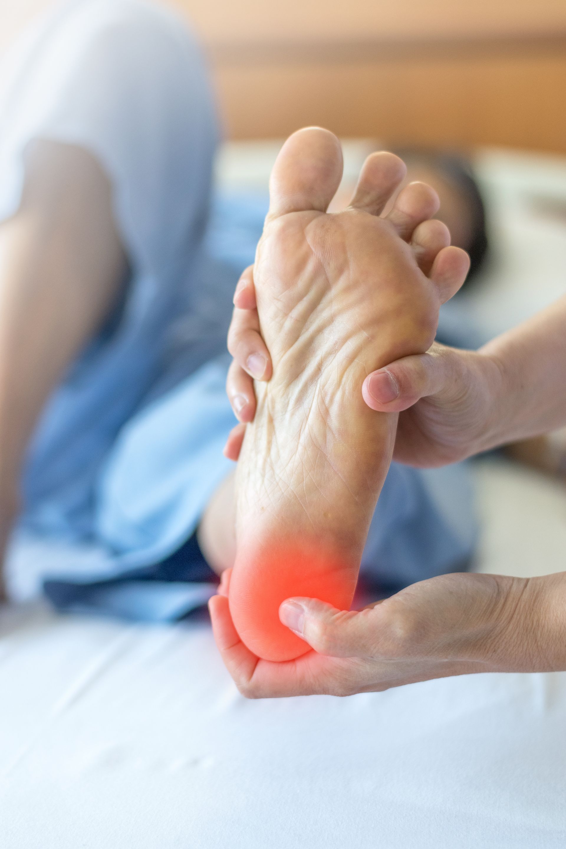 Person holding foot with red highlight on the heel, likely indicating pain, while lying in bed.