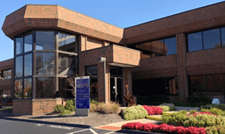 Brown brick office building with large windows and landscaping.