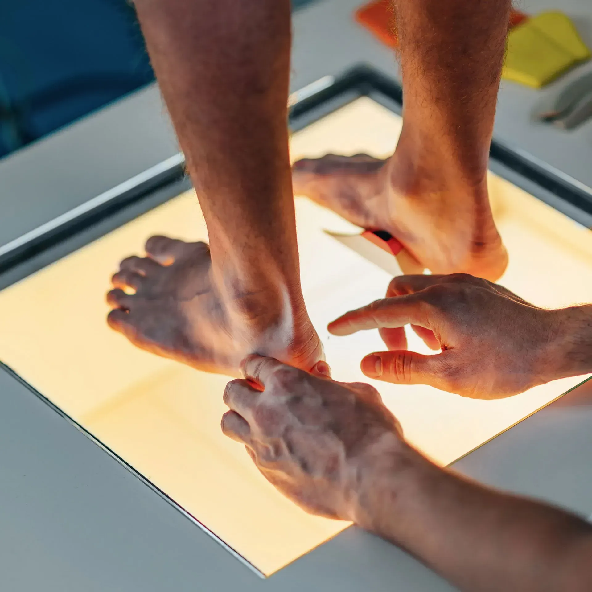 Feet being examined on a light box by hands, assessing foot structure and potential orthotic needs.