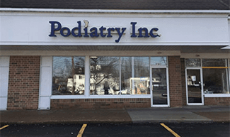 Podiatry Inc. storefront with blue lettering on a white awning. Brick facade, large windows.