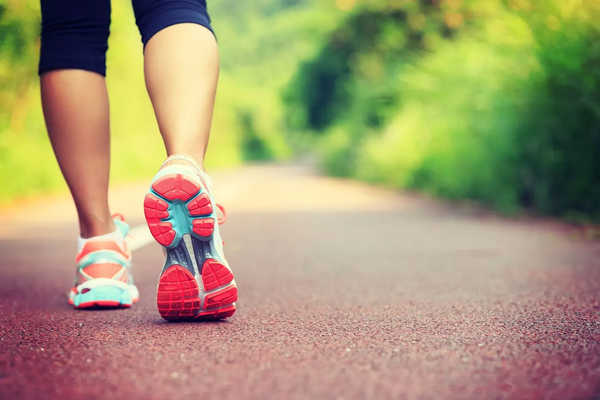 Person walking on a red path in running shoes, with green foliage in the background.