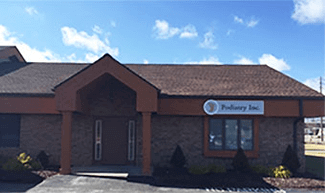 Exterior of Podiatry Inc. building with a brown roof, brown and tan brick, and a blue sky.