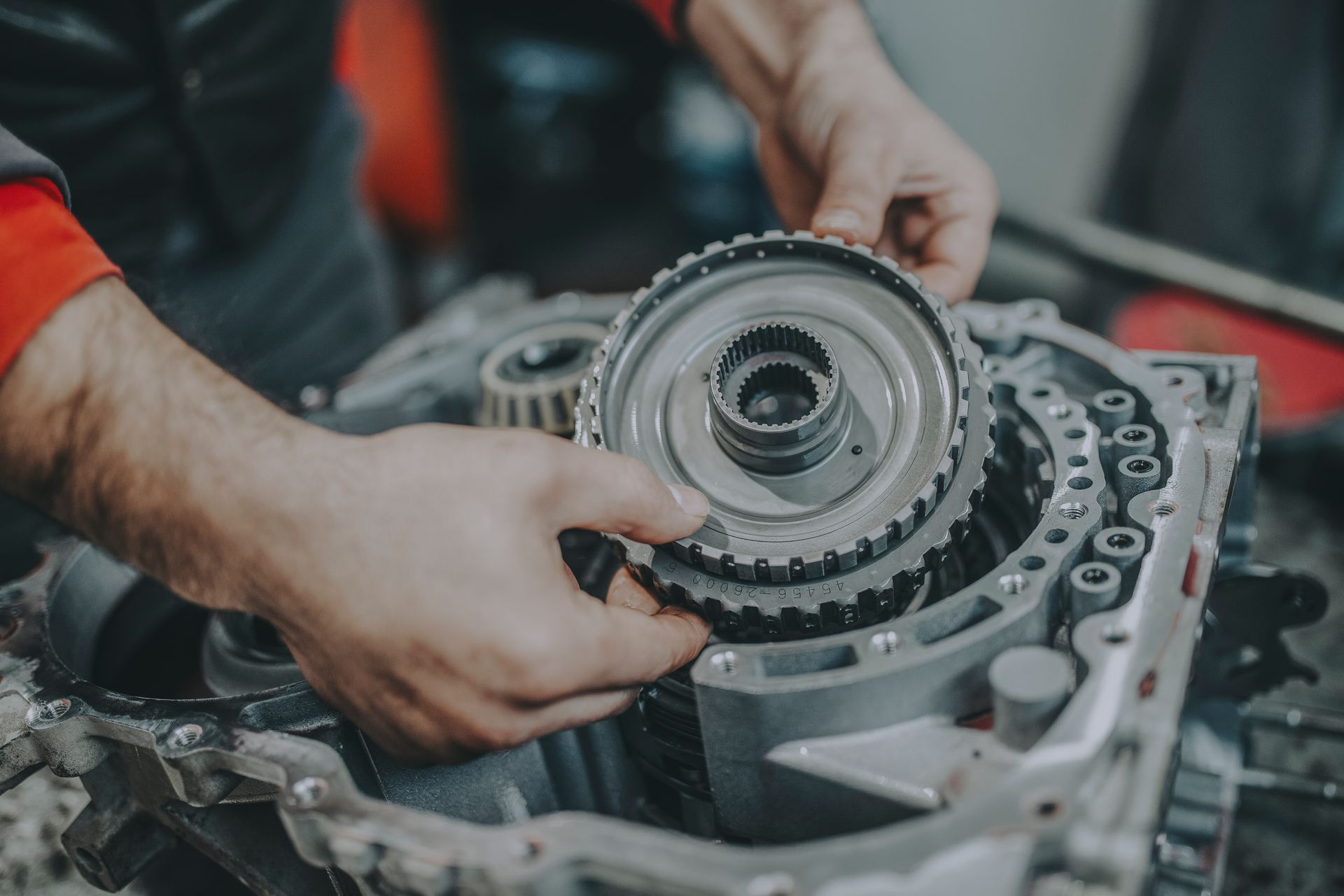 Hands assembling gears inside a car transmission.