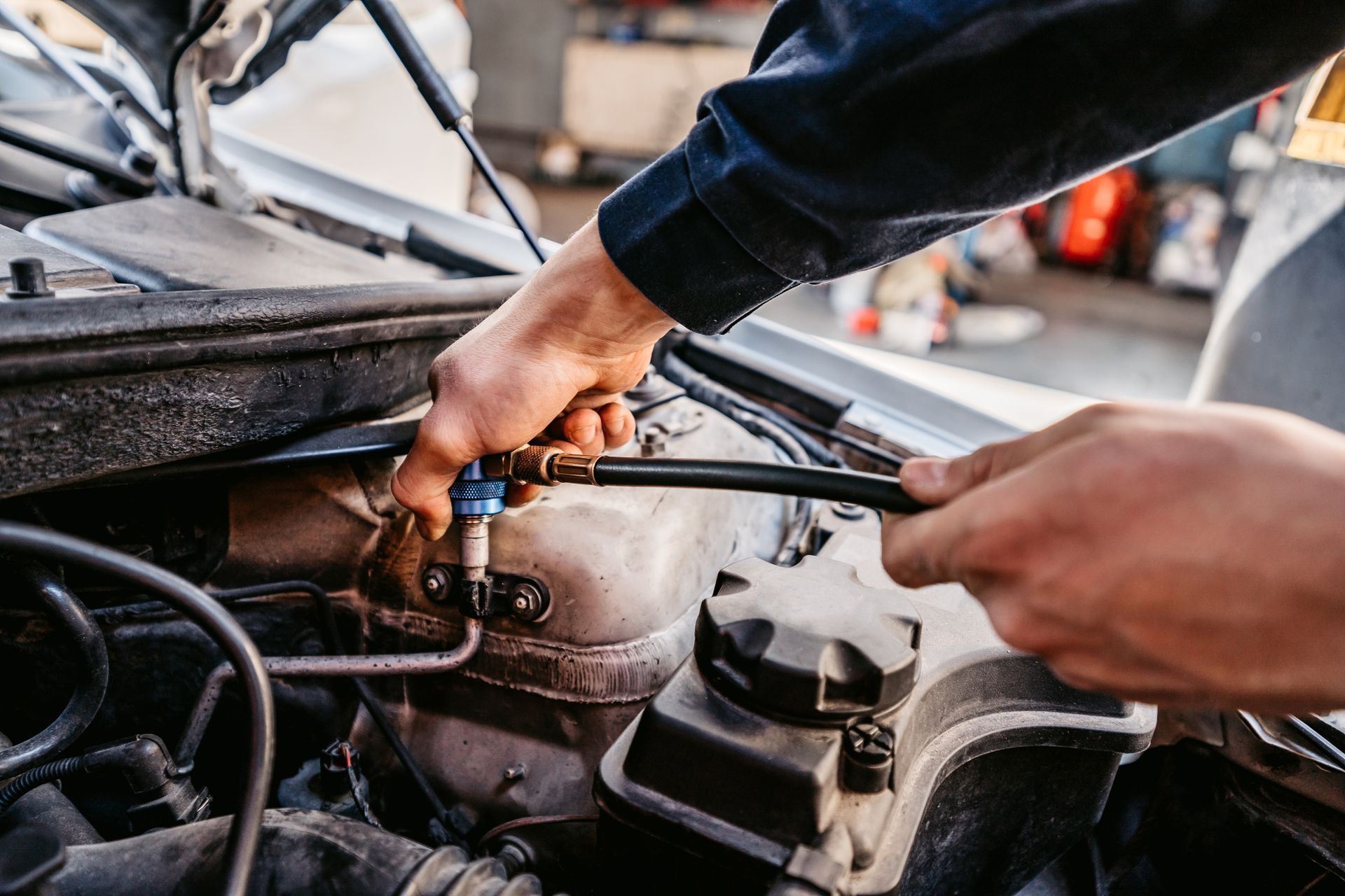 Mechanic connecting a hose to a car engine in a garage.