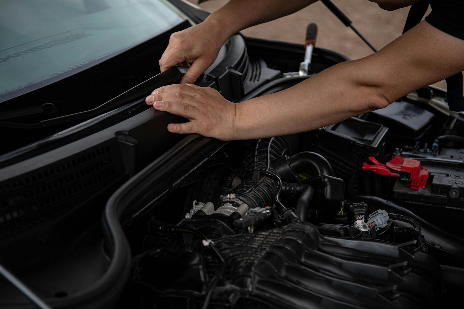 Person working on a car engine, inspecting the engine bay.