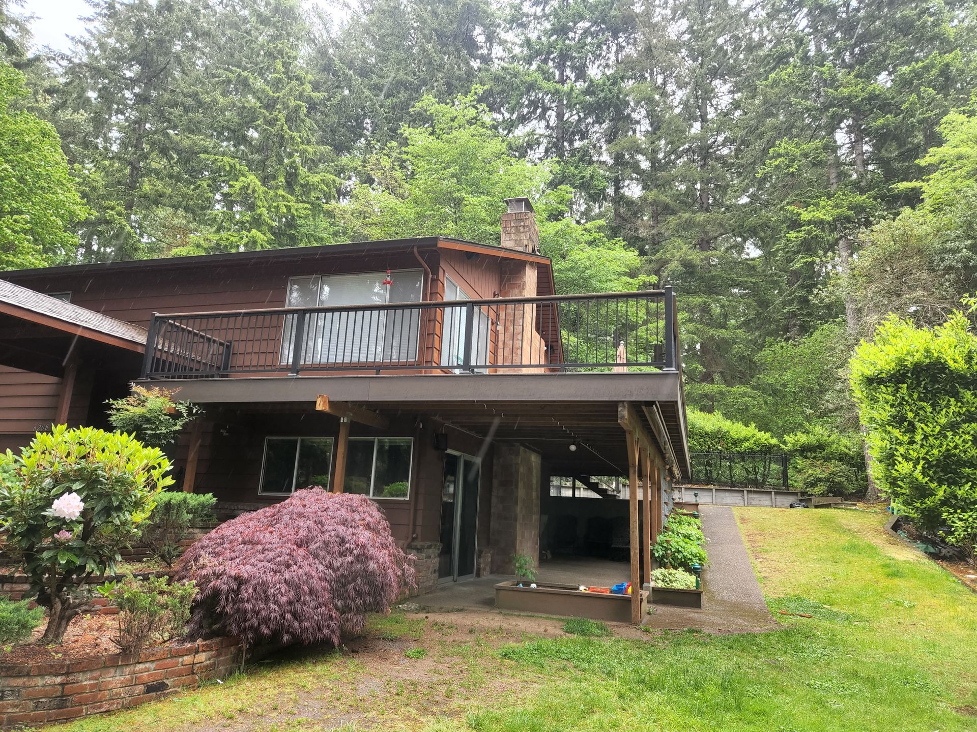 Brown house with a deck surrounded by trees and greenery.