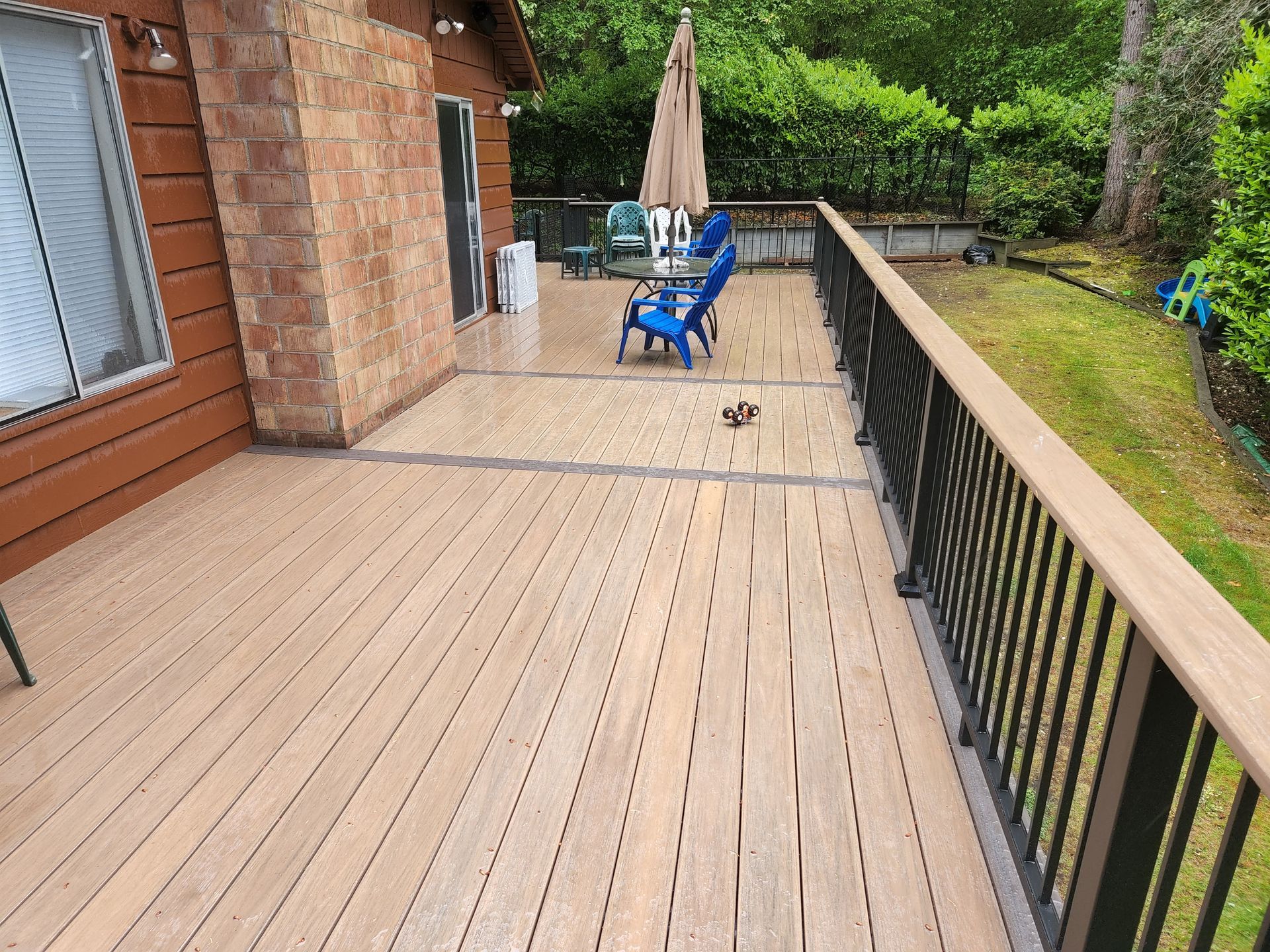 Wooden deck with black railing, brown siding, and outdoor furniture in a backyard.