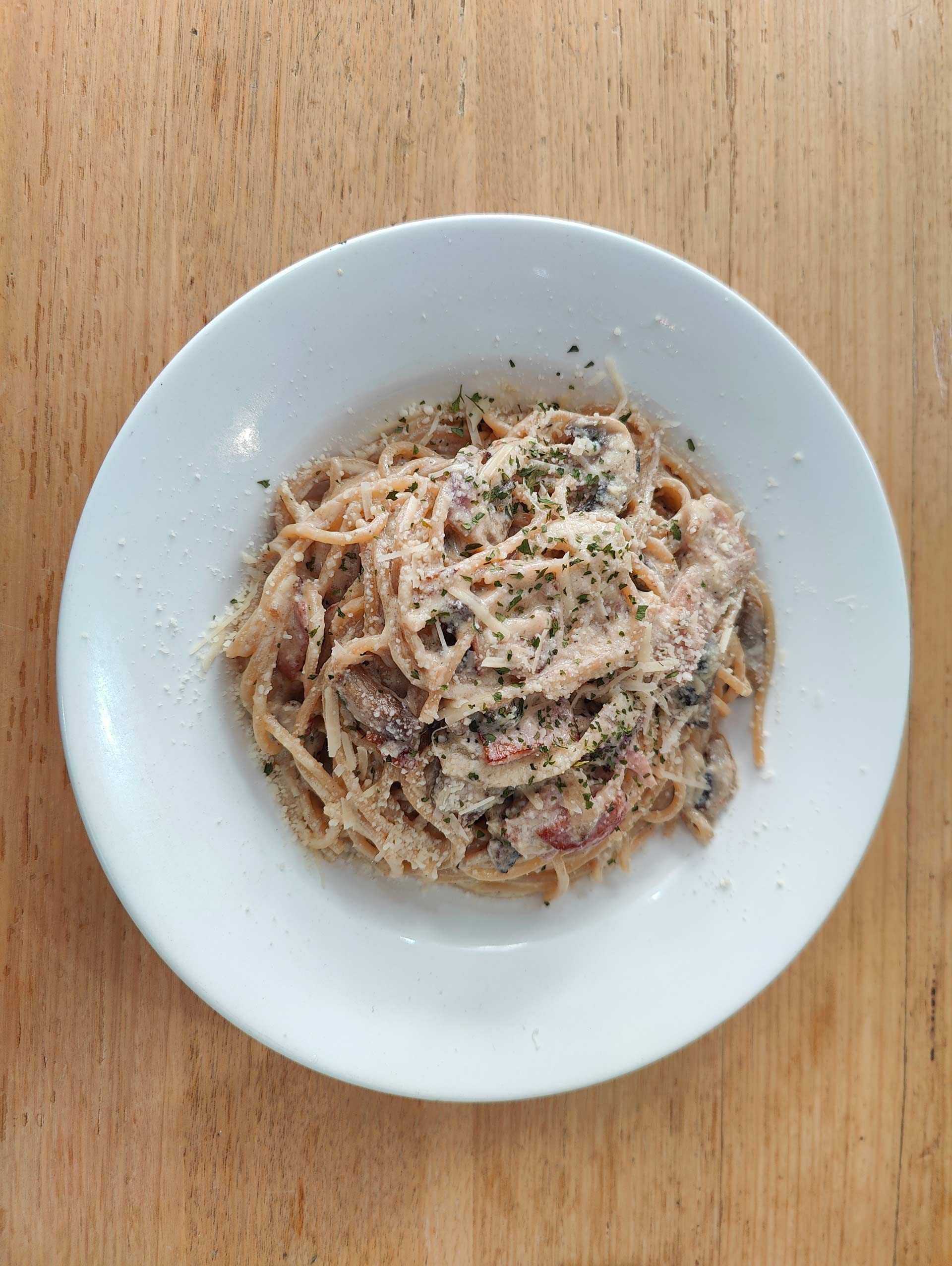 a white plate topped with spaghetti and mushrooms on a wooden table .