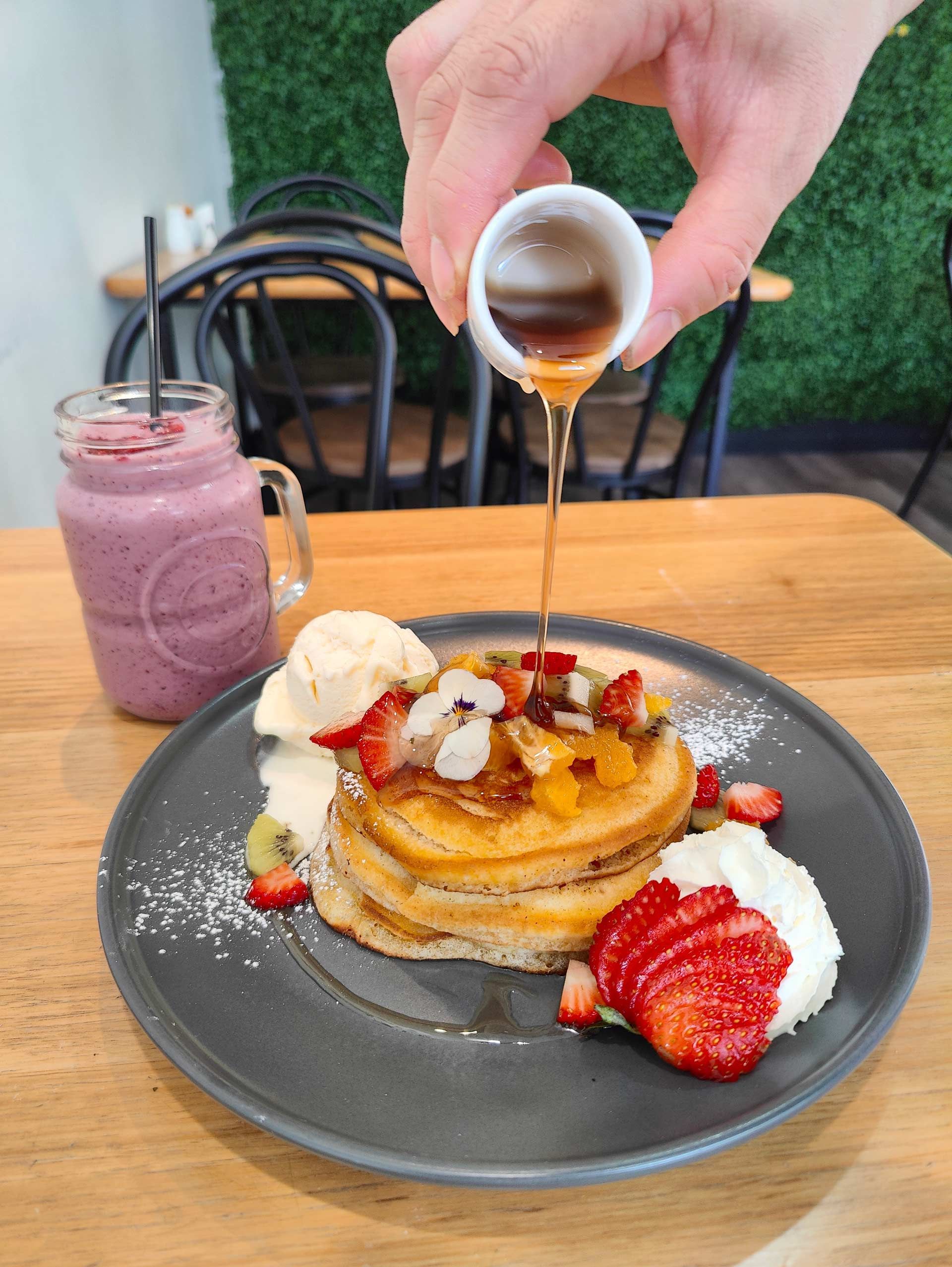 a person is pouring syrup on a stack of pancakes .