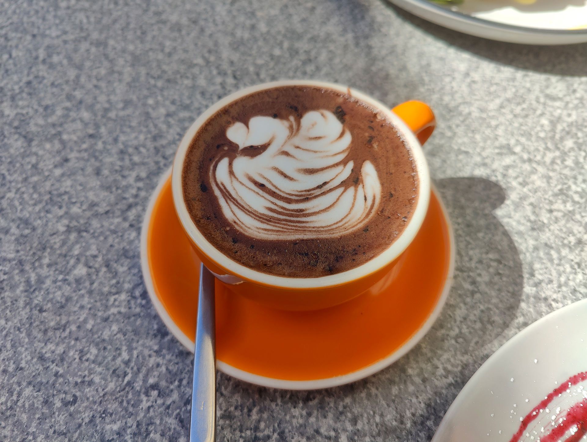 a cup of cappuccino with a spoon on a saucer on a table .