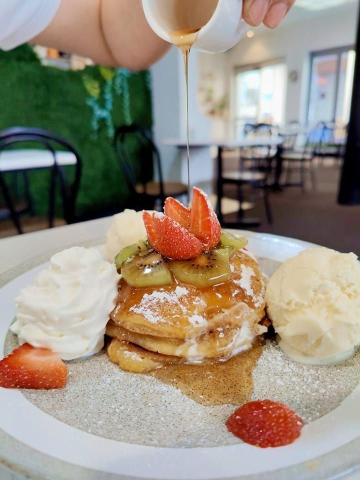 a person is pouring syrup on a stack of pancakes with whipped cream and fruit .