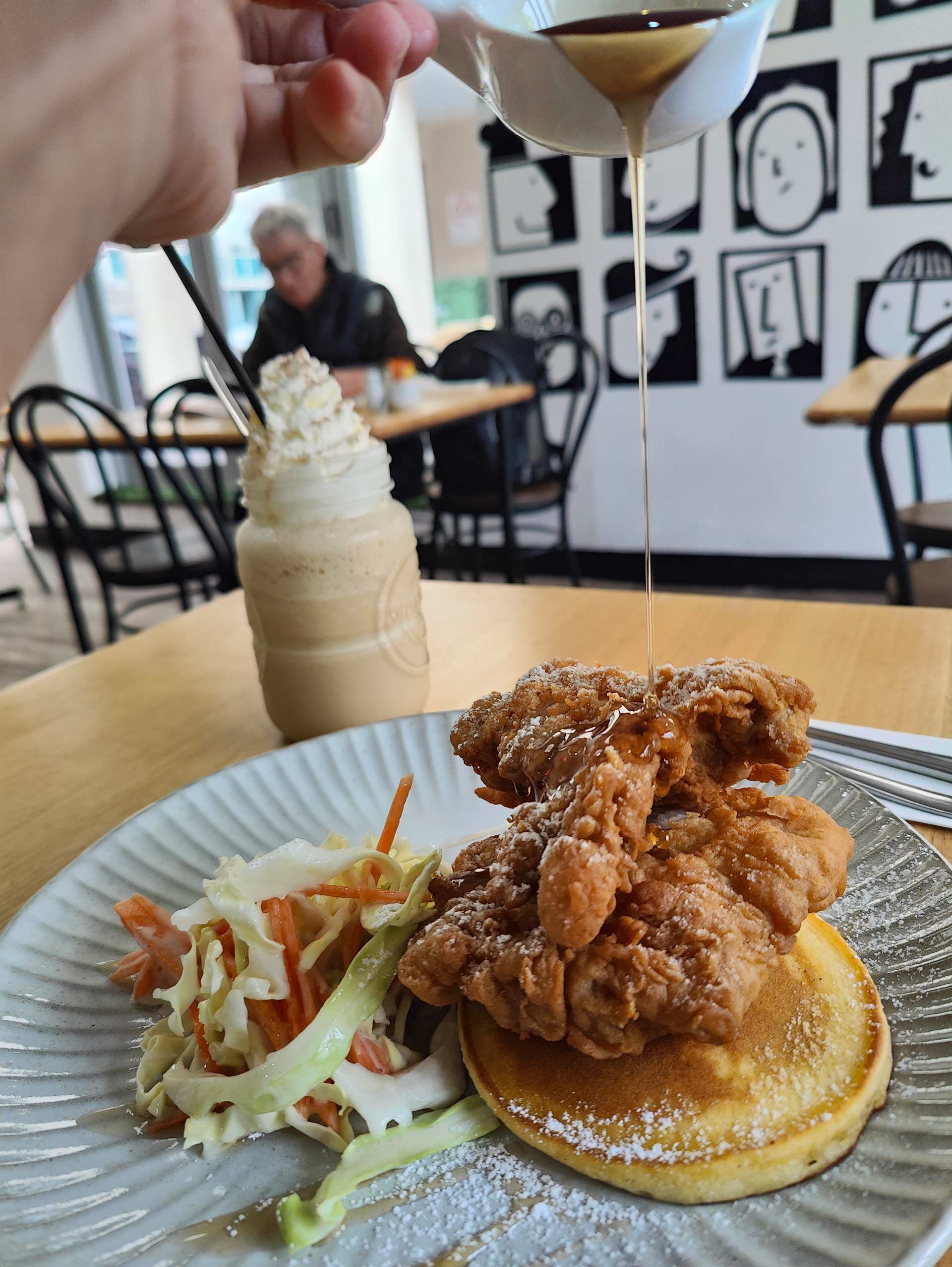 a person is pouring syrup on a pancake with fried chicken on top .