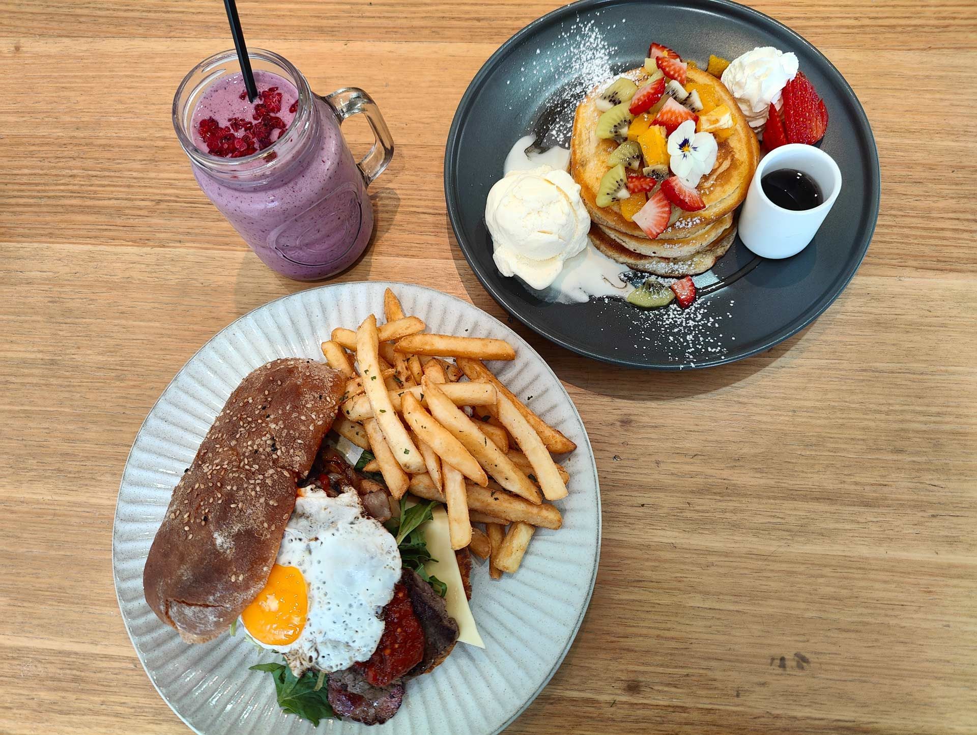 three plates of food and a drink are on a wooden table .