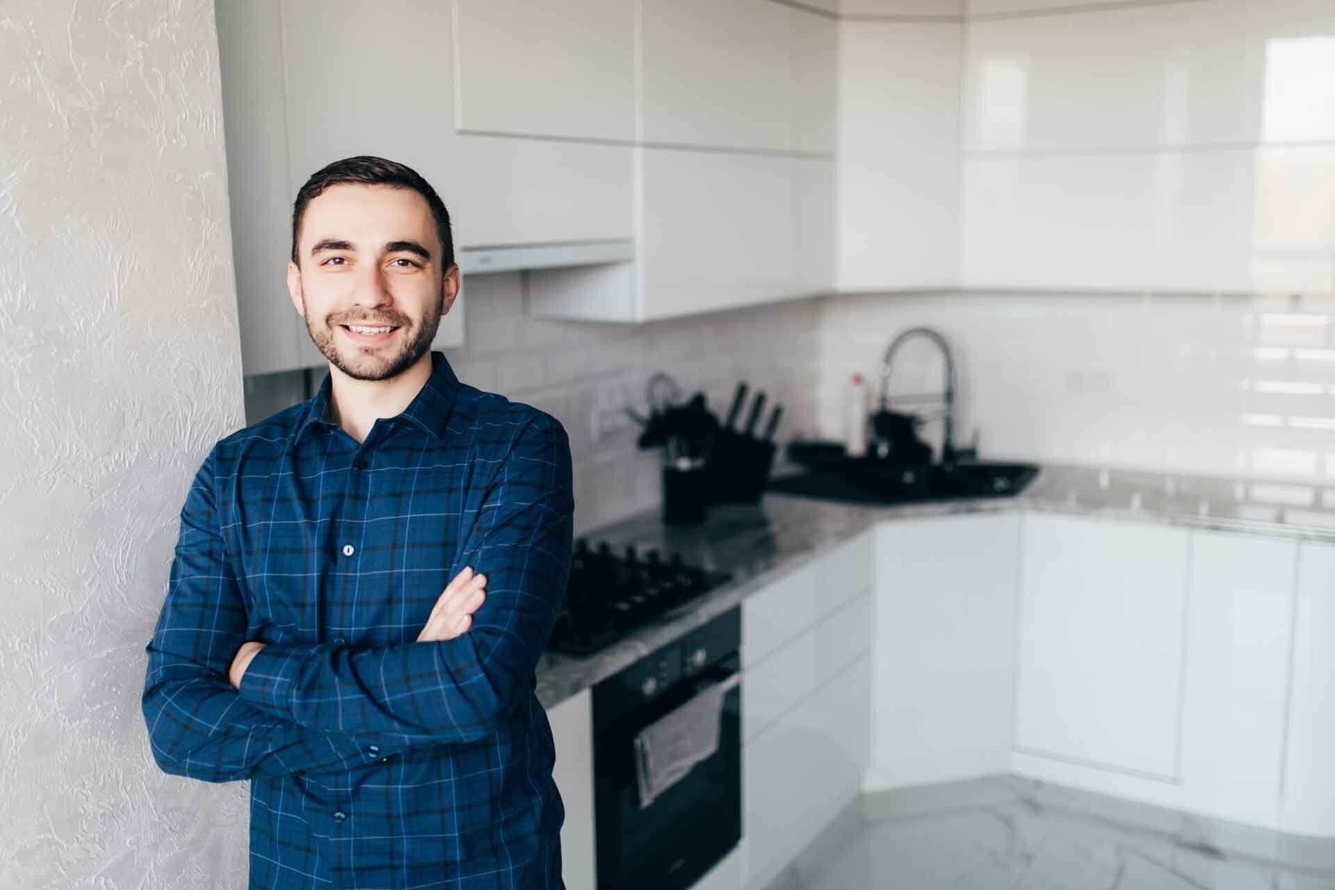 A man is standing in a kitchen with his arms crossed.