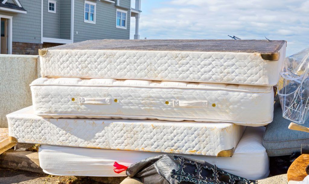 A stack of old mattresses piled up outdoors in front of a house.
