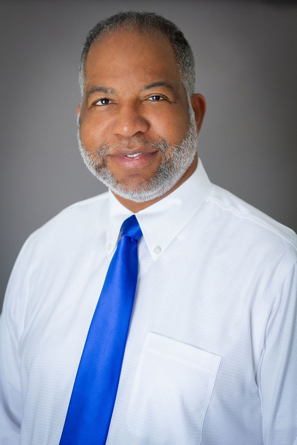 A man with a beard is wearing a white shirt and blue tie.