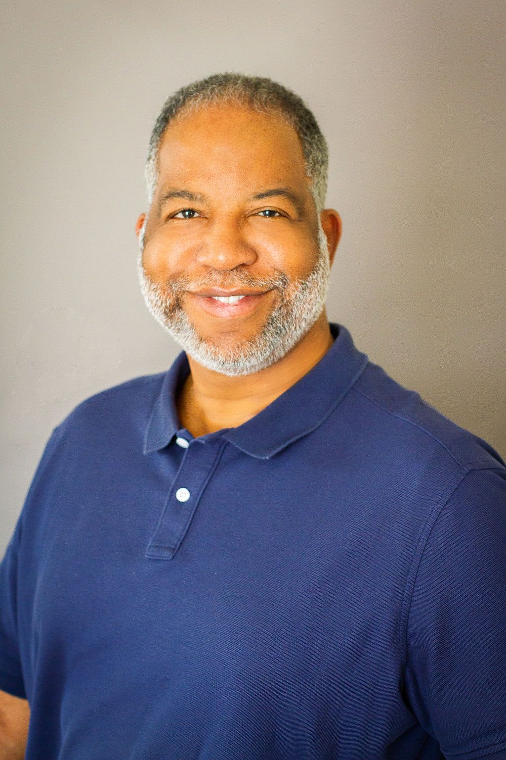 A man with a beard is wearing a blue polo shirt and smiling for the camera.