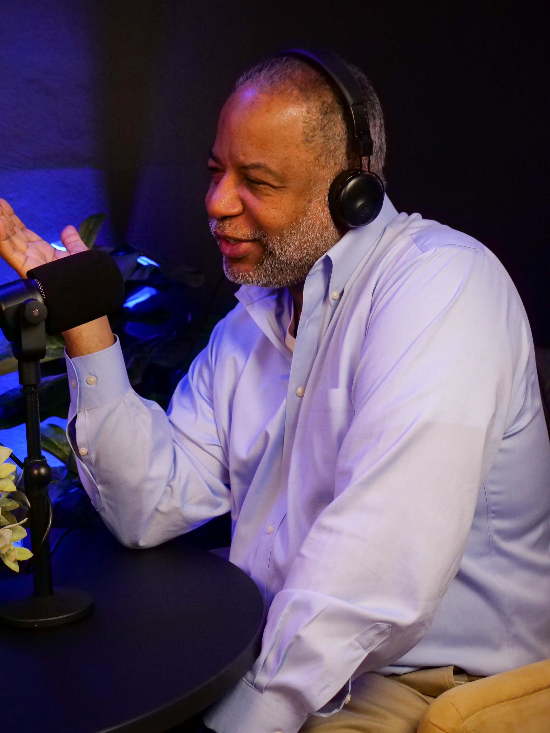 A man wearing headphones is sitting at a table talking into a microphone.