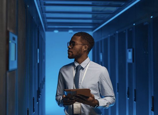 A man is holding a tablet in a server room.